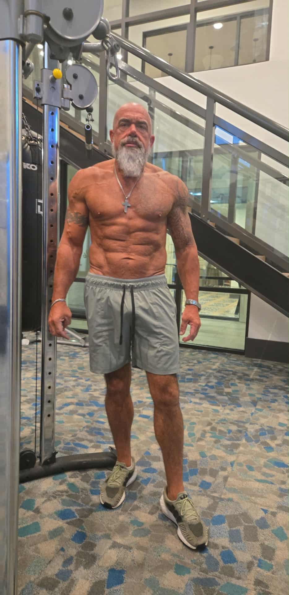 Hammer showcasing his incredible physique in gray shorts next to gym equipment, displaying visible abs and muscle definition
