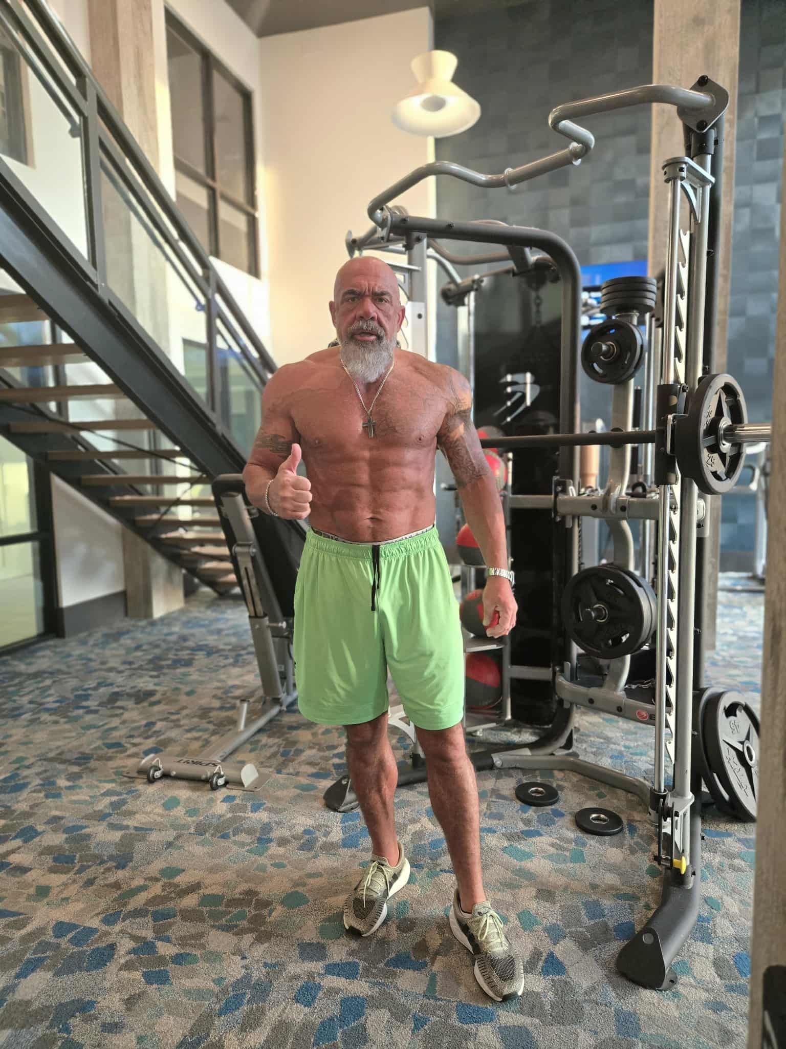 Hammer in bright green shorts giving a thumbs up next to gym equipment, showing his impressive transformation results